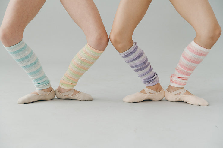 Ballet dancers wearing colorful striped leg warmers on a plain background