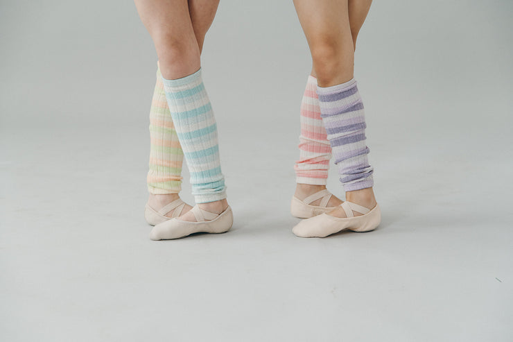 Pastel striped leg warmers worn with ballet shoes on a plain background