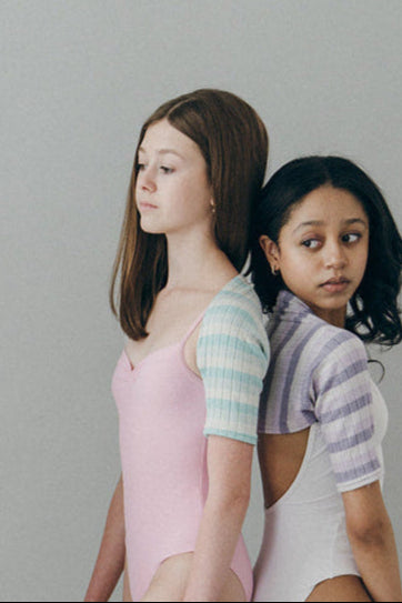 Four young ballerinas in pastel outfits posing against a gray background