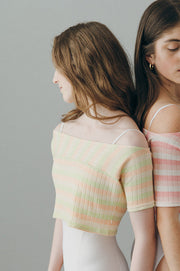Two women wearing colorful striped tops and white bottoms against a gray background