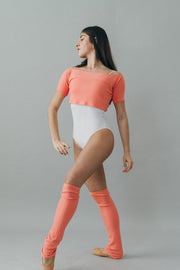 Woman wearing a cropped knit top, white leotard, and knee-high leg warmers on a plain background