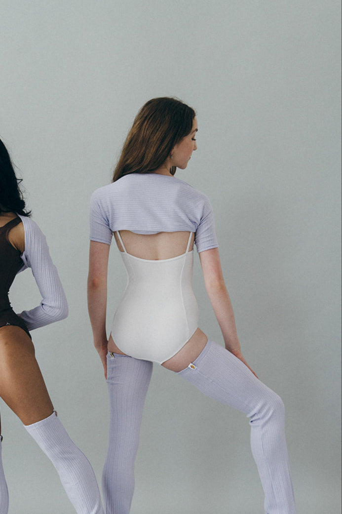 Dancer wearing purple shrug, a white leotard, and a thigh-high leg warmers.