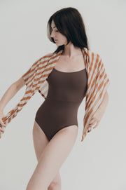 Woman wearing a brown leotard with a striped cover-up against a plain background