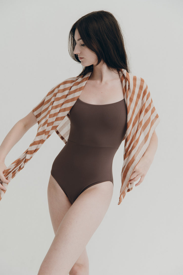 Woman wearing a brown leotard with a striped cover-up against a plain background