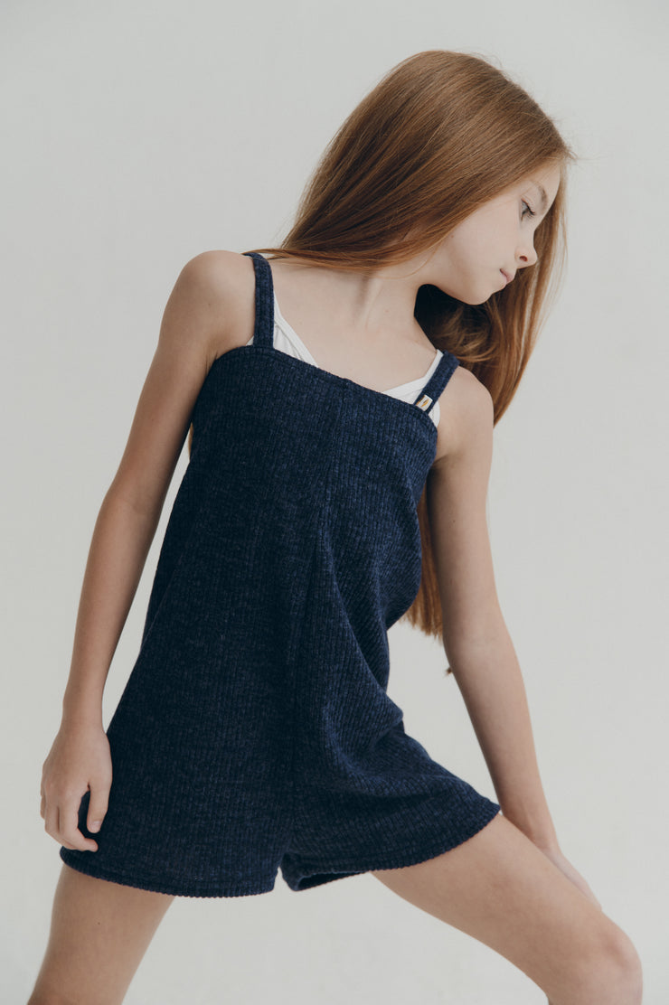 Dancer wearing a navy blue romper with thin straps on a plain background