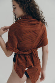 Woman wearing a rust-colored knitted shawl on a plain background