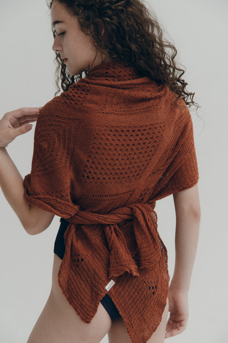 Woman wearing a rust-colored knitted shawl on a plain background