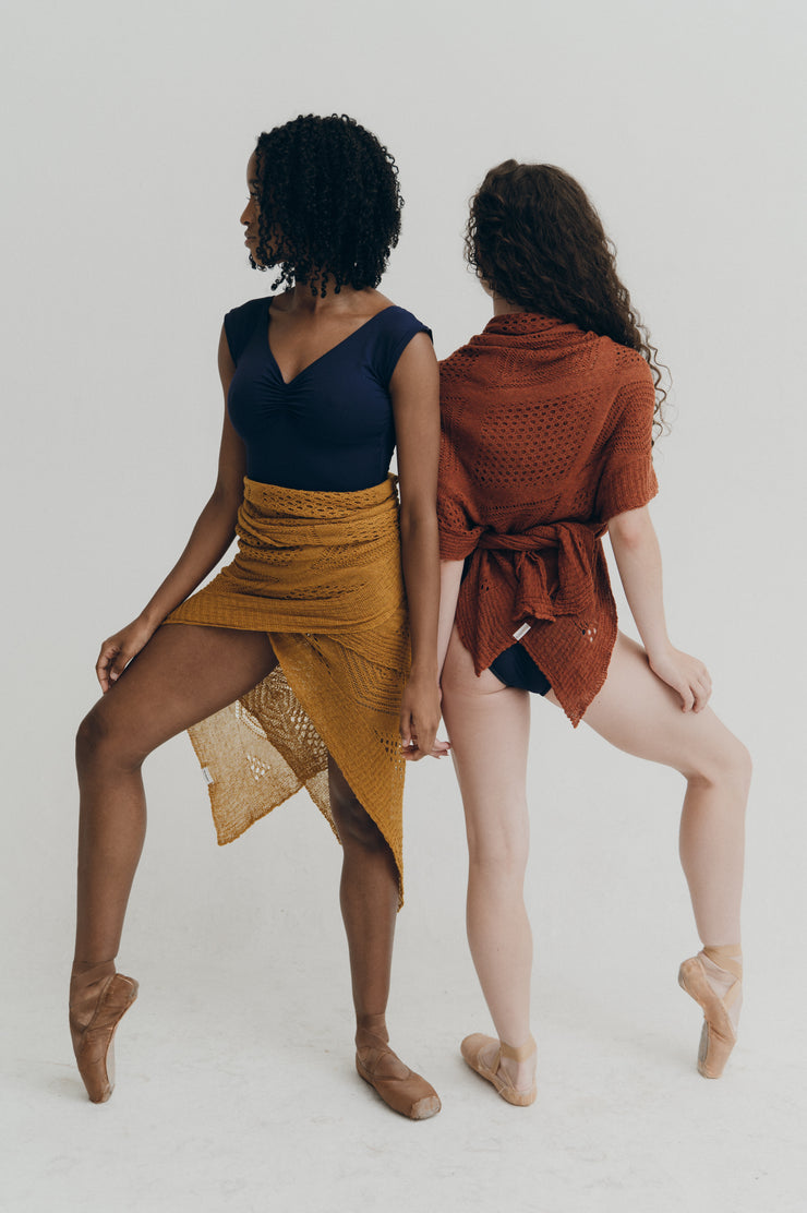Two women in dance attire standing back-to-back on a plain background