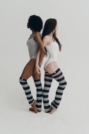 Two women wearing striped knee-high leg warmers on a plain background