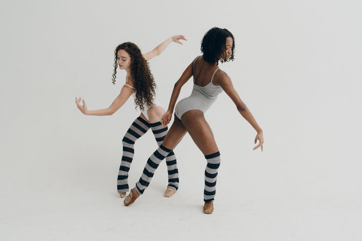 Two women wearing striped knee-high leg warmers on a plain background