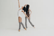 Two women in matching outfits with striped leg warmers against a white background