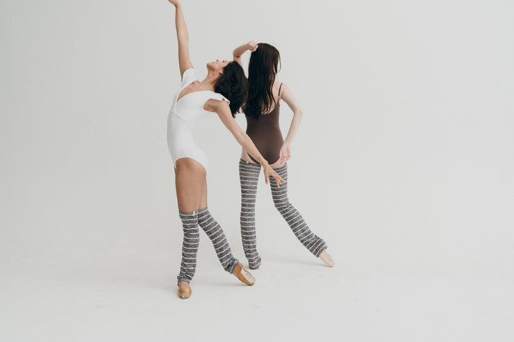 Two women in matching outfits with striped leg warmers against a white background
