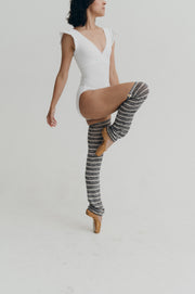 Person wearing a white leotard and striped knee-high leg warmers on a plain background