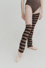 Person wearing brown leotard and striped knee-high leg warmers on a light gray background