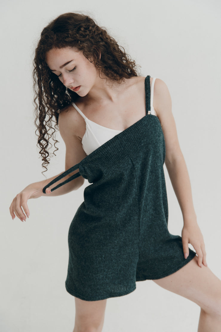 Woman wearing a dark green romper over a white leotard on a plain background