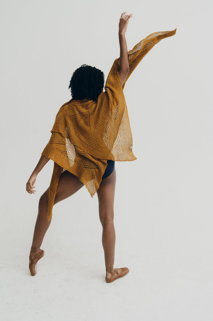 Person wearing a yellow knitted shawl on a plain background