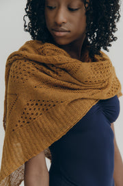 Woman wearing a gold knitted shawl over a blue leotard against a neutral background